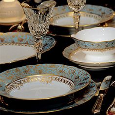 a table topped with plates and silverware on top of a black table covered in gold trimmings