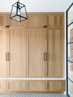 an empty room with wooden cupboards and tiled flooring on the walls, along with a hanging light fixture