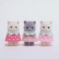 three small stuffed animals are standing next to each other on a white surface and one is wearing a pink dress