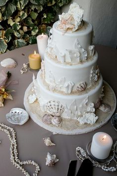 a white wedding cake with seashells and candles on the table next to it