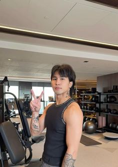 a man standing in front of a gym machine giving the peace sign with his hand