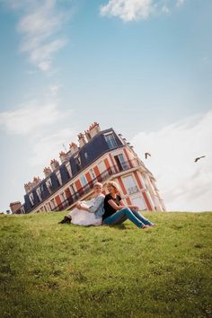 two people sitting on the grass in front of a large building with many windows and balconies