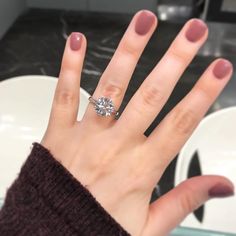 a woman's hand with a diamond ring on her left hand and a white plate in the background