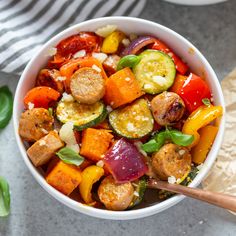 a white bowl filled with vegetables on top of a table next to a wooden spoon