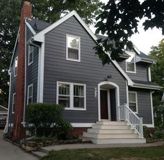 a gray house with white trim on the front door and stairs leading up to it