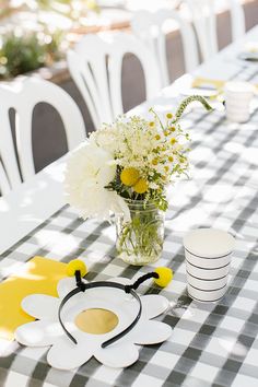 the table is set with white and yellow flowers in a vase, plates, and napkins