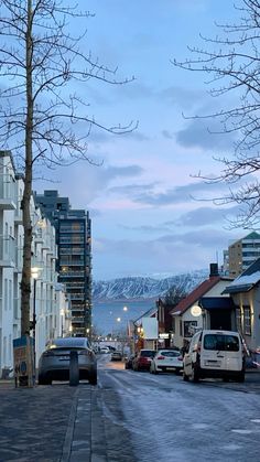 cars parked on the side of a street next to tall buildings and snow covered mountains