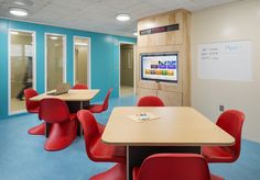 a room with several tables and red chairs in front of a white board on the wall