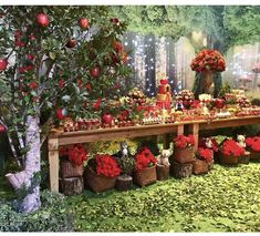 a table covered in lots of red flowers and apples next to a forest scene with trees