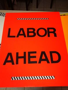 an orange sign that says labor ahead on the floor next to a black and white striped table cloth