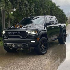 a black truck parked on the side of a road next to trees and water in front of it