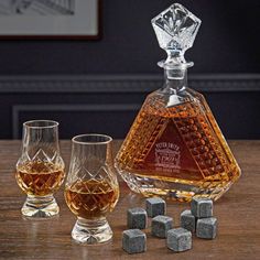 three glasses and one decanter sitting on a table next to some whiskey cubes