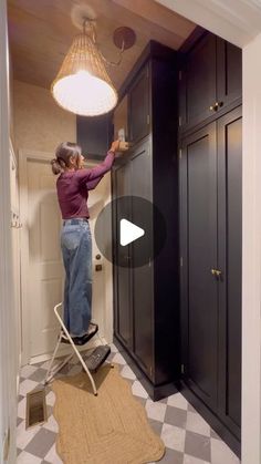 a woman standing on top of a stepladder in a kitchen next to cabinets