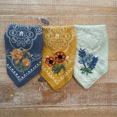 three bandannas with flowers on them sitting on a wooden surface, one is blue and the other has yellow