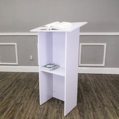 a white book shelf with an open book on top and a magazine rack underneath it