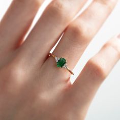 a woman's hand with a green ring on top of her finger and an emerald in the middle