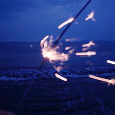 some sparklers are in the air near the water and beach at night with blue sky