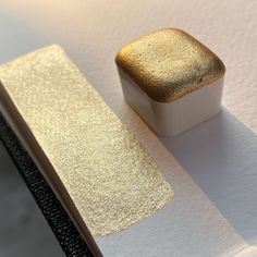 a square piece of gold foil sitting on top of a white surface next to a metal object