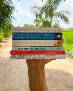 a person holding up a stack of books in front of their face and palm trees