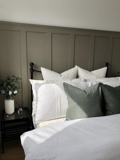 a white bed topped with lots of pillows next to a night stand and vase filled with flowers