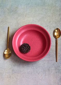 a pink plate with a pine cone on it and two gold spoons next to it