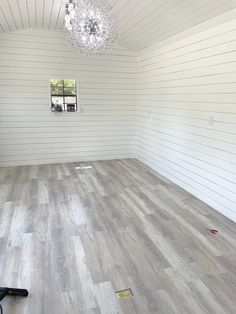 an empty room with white walls and wood flooring, including a chandelier