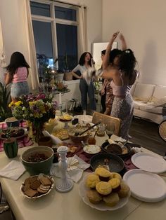 two women are standing in front of a table full of food and desserts,