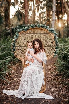 a woman holding a baby in her arms while sitting on a wicker chair surrounded by trees