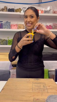 a woman holding scissors in front of a wooden box with writing on it and she is smiling at the camera