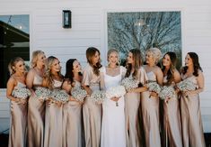 a group of women standing next to each other in front of a white building holding bouquets