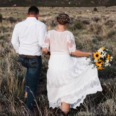 a man and woman walking through a field holding hands