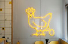 the neon chicken sign is on the wall in the kitchen, next to two yellow chairs