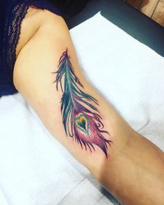 a woman's leg with a tattoo on it that has a colorful peacock feather