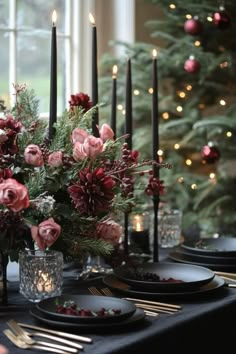 the table is set with black plates, silverware and flowers in glass vases