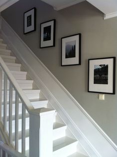 some pictures are hanging on the wall next to a stair case with white railings