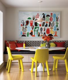 a dining room table with yellow chairs and a painting on the wall behind it,