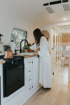 a woman in a white dress is standing at the counter and looking into an oven