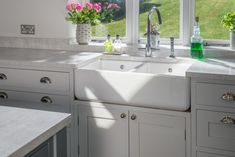 a white kitchen sink sitting under a window next to a green vase filled with flowers