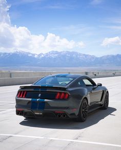 the rear end of a gray sports car driving on a road with mountains in the background