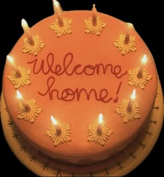 a welcome home cake with lit candles on the top and words written in orange frosting