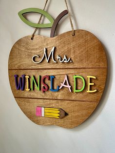 a wooden sign that says, mrs winslade and has an apple shaped with pencils hanging from it