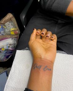 a woman's hand with two small tattoos on her left wrist and the word self care written in cursive writing