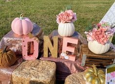 pumpkins, flowers and other decorations are sitting on hay bales in front of a sign that says one