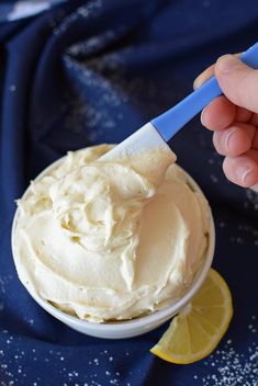 a hand holding a blue handled spoon over a bowl of whipped cream and lemon wedges