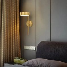 a bed sitting next to a window with curtains on top of it and a lamp hanging from the wall