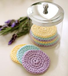 four crocheted coasters sitting on top of a table next to a flower