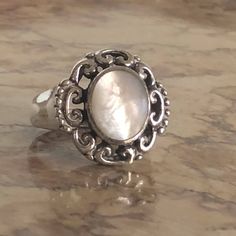 This sterling silver ring feels good and solid and heavy on your finger. It has a 10mm x 12mm oval faux mother of pearl/moonstone cabochon that almost has a cats-eye look, with a pretty pearliness to it. It is surrounded by elaborate scrollwork and flat beading on the shoulders. It is size 6.5 and comes in a colorful presentation box. Vintage Silver Oval Pearl Ring, Elegant Oval Nickel-free Moonstone Ring, Elegant Oval Moonstone Nickel-free Ring, Silver Oval Mother Of Pearl Rings, Silver Oval Rings With Mother Of Pearl, Adjustable Elegant Moonstone Ring Oval Cabochon, Elegant Oval Cabochon Moonstone Ring Stamped 925, Vintage Turquoise Ring, Mother Of Pearl Ring