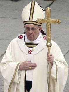 a man in a priest's outfit holding a cross and walking down the street