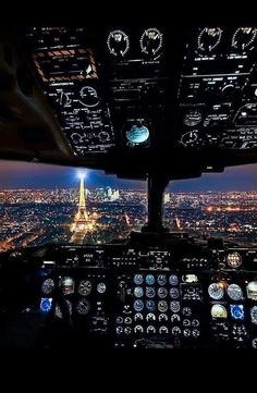 an airplane cockpit with the lights on at night and city lights visible in the background