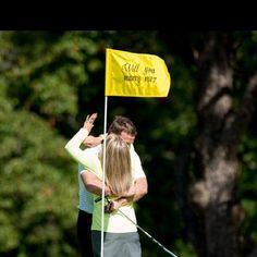 a man and woman standing next to each other near a yellow flag on a golf course